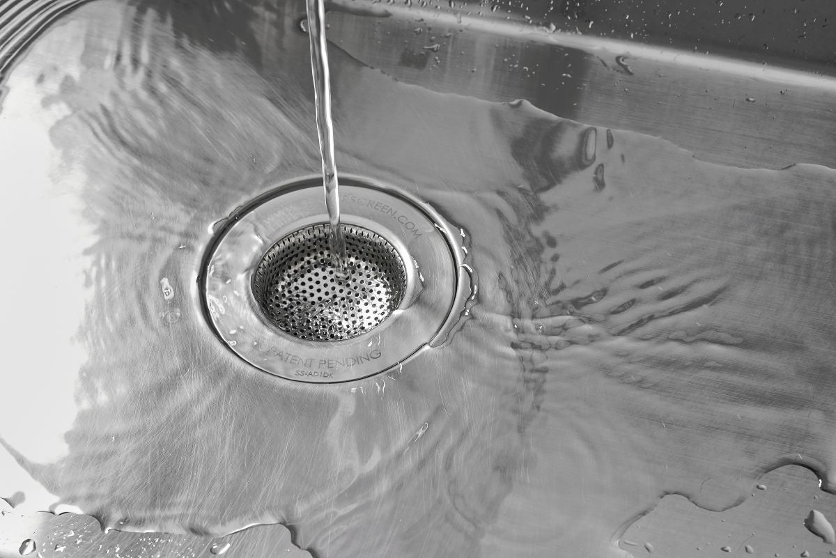 Close-up of water flowing into a sink drain protected by a SemperScreen® permanent sink screen.