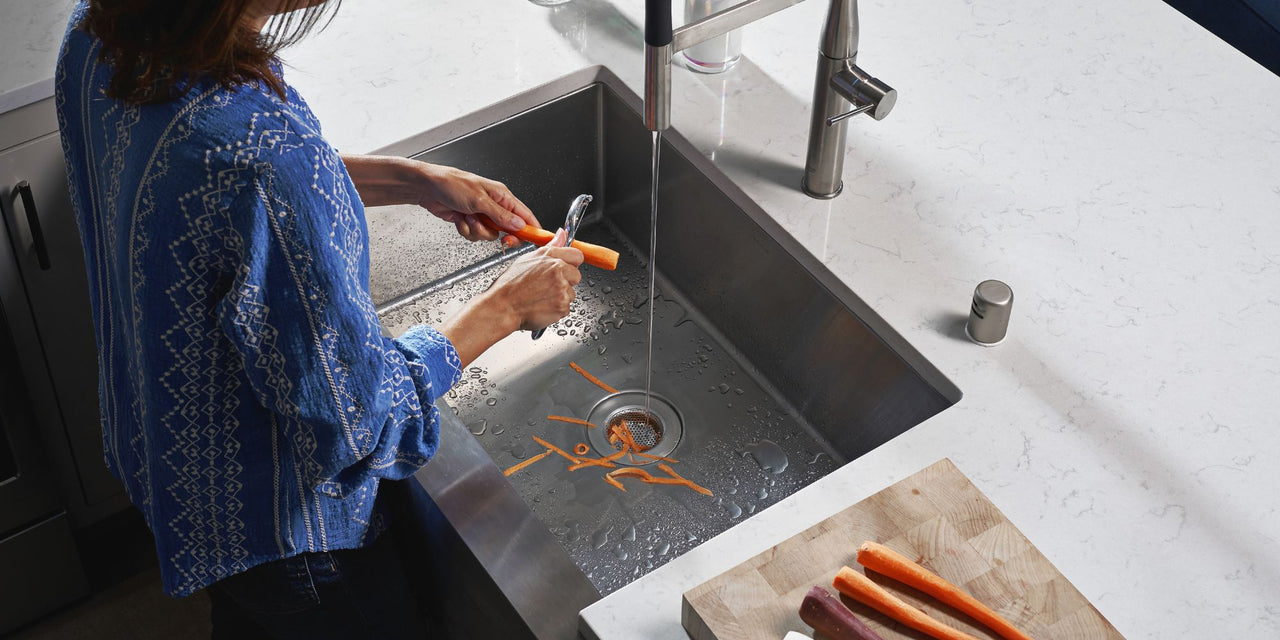 Person standing in front of a kitchen sink peeling a carrot with a SemperScreen® permanent sink screen protecting the carrot shavings from entering the kitchen plumbing drains