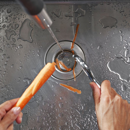 SemperScreen® permanent sink screen installed in a stainless kitchen sink with carrot peels staying in the sink and not going down the drain.